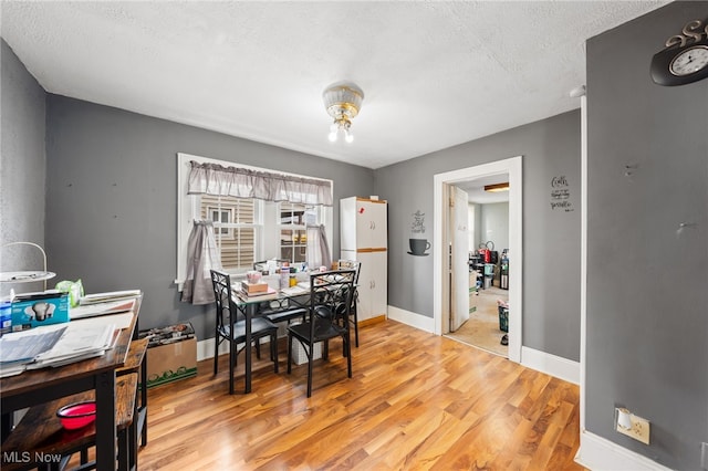 dining space with light wood-type flooring, baseboards, and a textured ceiling