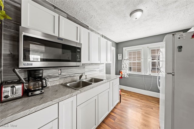 kitchen with light wood finished floors, stainless steel microwave, freestanding refrigerator, white cabinets, and a sink