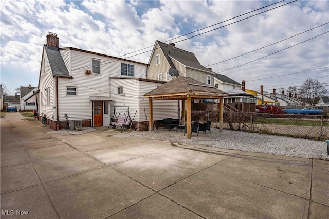 rear view of house featuring central AC, fence, a gazebo, a residential view, and a chimney