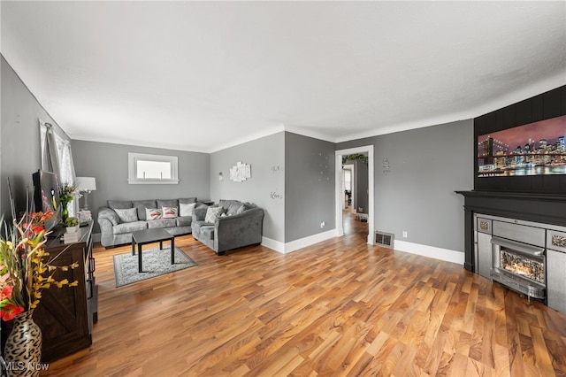 living area featuring a glass covered fireplace, visible vents, baseboards, and wood finished floors