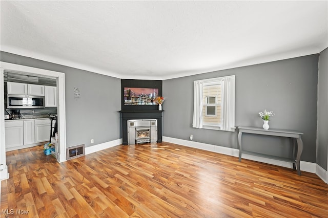 unfurnished living room featuring baseboards, a fireplace, visible vents, and light wood-type flooring