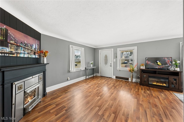 living room featuring visible vents, a textured ceiling, wood finished floors, a glass covered fireplace, and baseboards