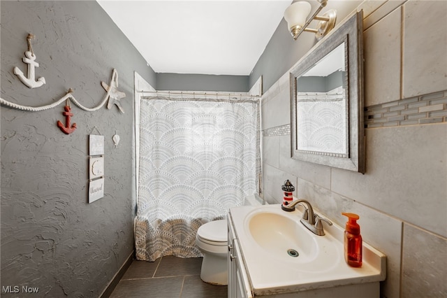 full bath featuring vanity, tile patterned flooring, tile walls, toilet, and a textured wall