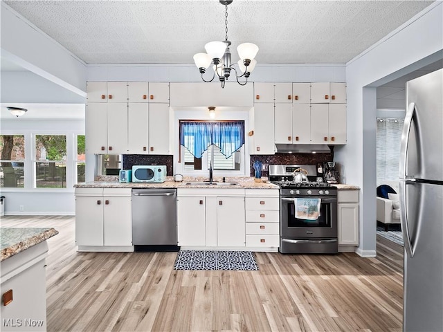 kitchen with a sink, tasteful backsplash, appliances with stainless steel finishes, white cabinets, and an inviting chandelier