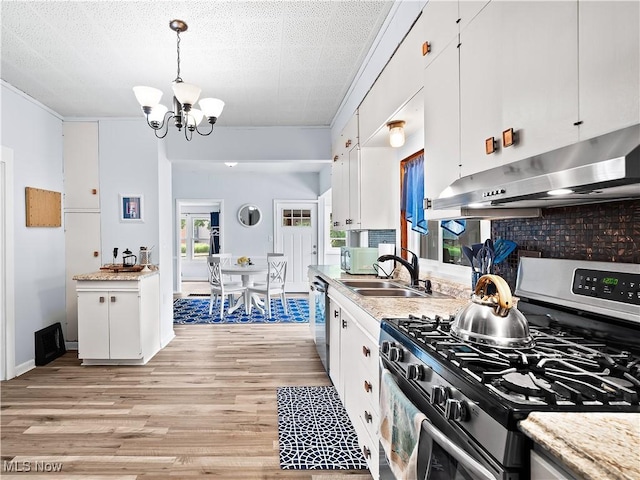 kitchen with under cabinet range hood, light wood-style flooring, stainless steel appliances, an inviting chandelier, and white cabinetry