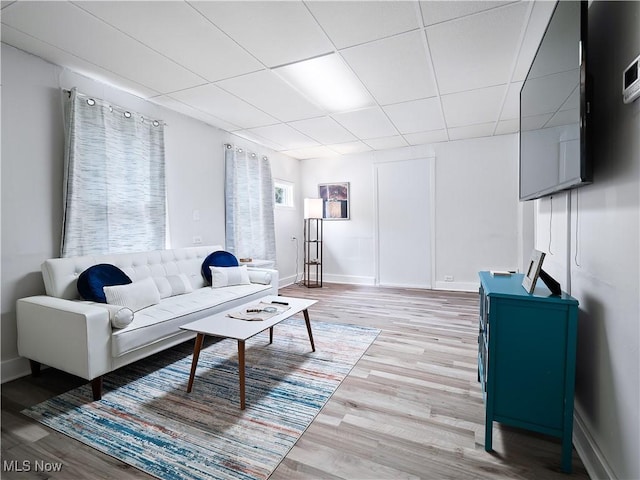 living room featuring a drop ceiling, baseboards, and light wood-style floors