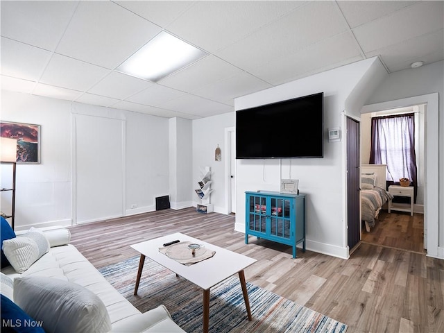 living room featuring light wood-style flooring, a paneled ceiling, and baseboards