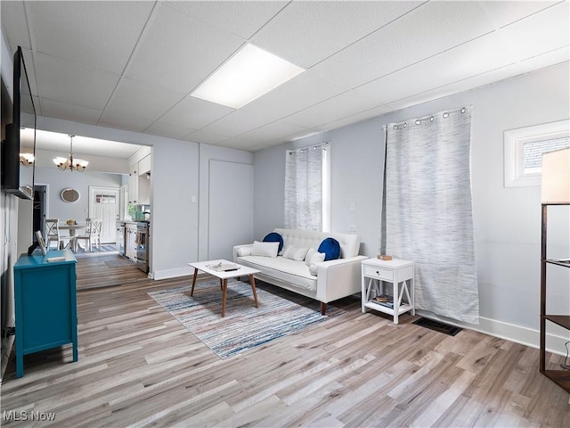 living room with light wood finished floors, baseboards, a paneled ceiling, and an inviting chandelier