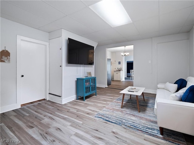 living area with a paneled ceiling, wood finished floors, baseboards, and a chandelier