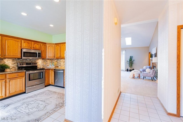 kitchen with light tile patterned flooring, backsplash, appliances with stainless steel finishes, and brown cabinetry