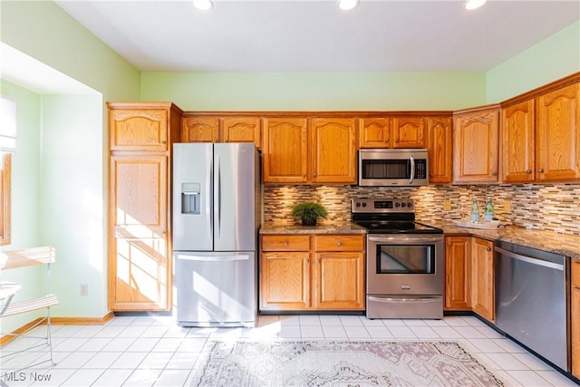 kitchen featuring light tile patterned floors, decorative backsplash, brown cabinets, appliances with stainless steel finishes, and stone countertops