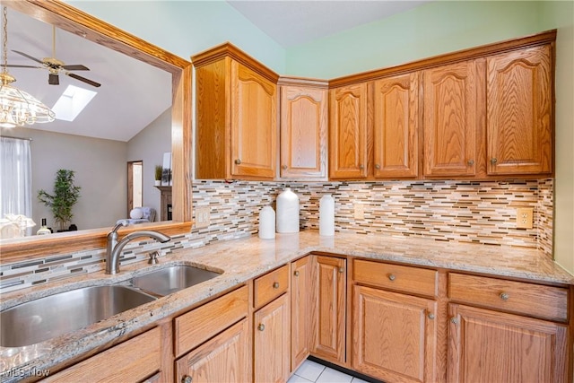 kitchen with lofted ceiling with skylight, a ceiling fan, a sink, backsplash, and light stone countertops