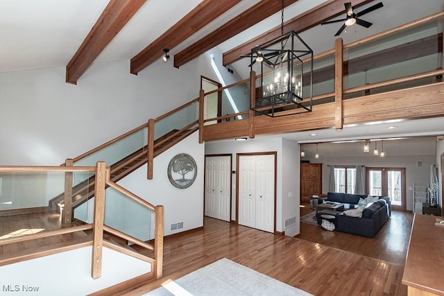 unfurnished living room with stairway, ceiling fan with notable chandelier, high vaulted ceiling, and wood finished floors