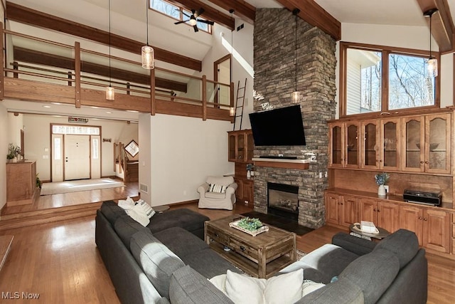 living area with beam ceiling, high vaulted ceiling, light wood-style flooring, a fireplace, and baseboards