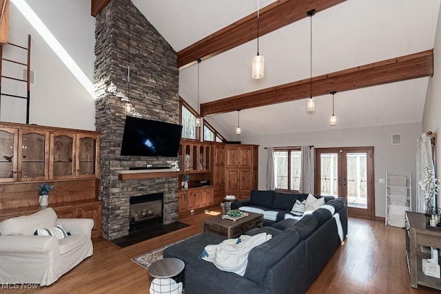 living area featuring wood finished floors, high vaulted ceiling, beam ceiling, a stone fireplace, and french doors