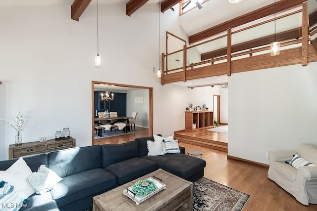 living area with wood finished floors, baseboards, high vaulted ceiling, an inviting chandelier, and beam ceiling