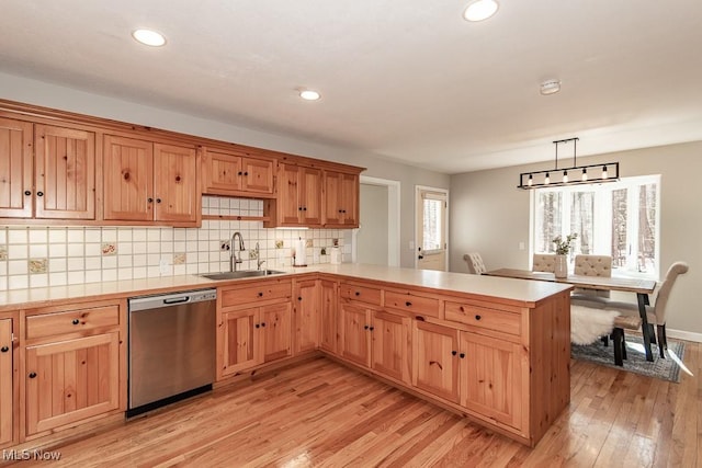 kitchen featuring light wood-style flooring, a sink, stainless steel dishwasher, a peninsula, and decorative backsplash