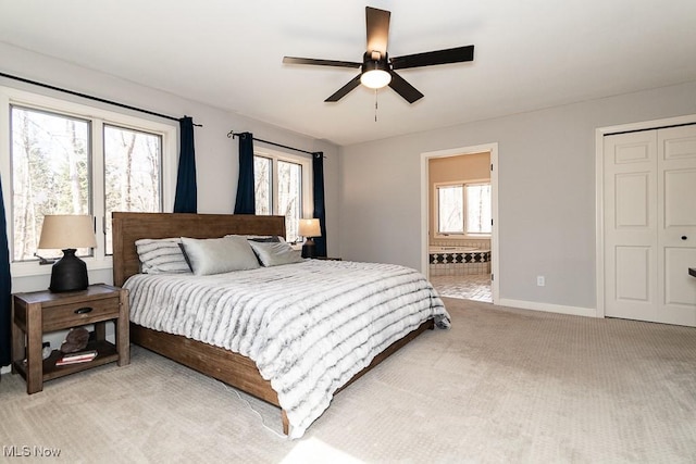 bedroom featuring connected bathroom, a closet, baseboards, light colored carpet, and ceiling fan