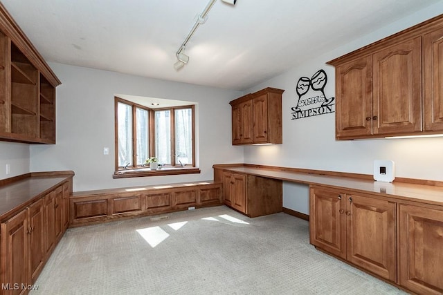 kitchen featuring open shelves, track lighting, brown cabinetry, and built in study area