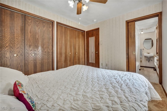 carpeted bedroom with multiple closets, a sink, connected bathroom, wallpapered walls, and ceiling fan