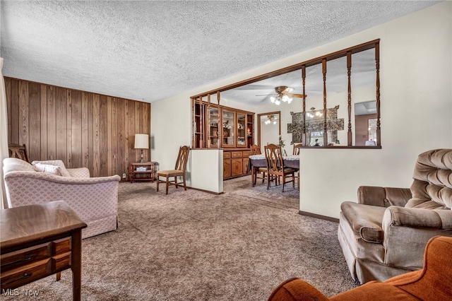 carpeted living area with a textured ceiling, wooden walls, and ceiling fan