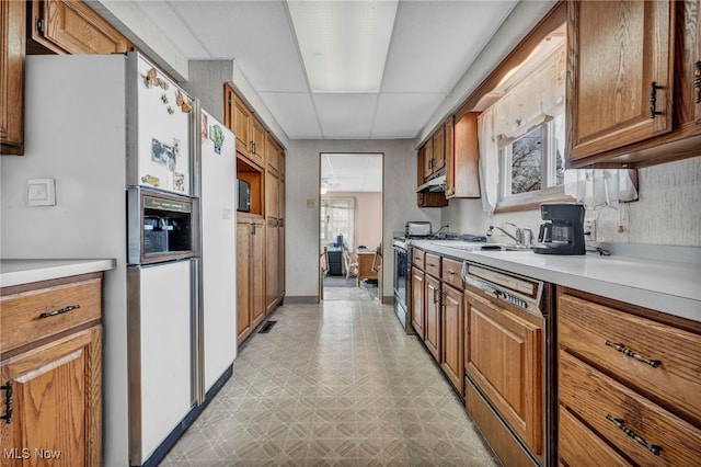 kitchen with gas range, dishwasher, light floors, brown cabinets, and white refrigerator with ice dispenser