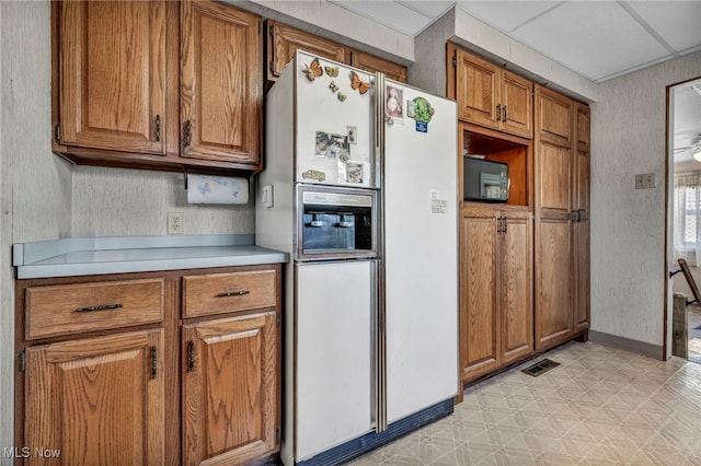 kitchen featuring light floors, visible vents, light countertops, white fridge with ice dispenser, and brown cabinets