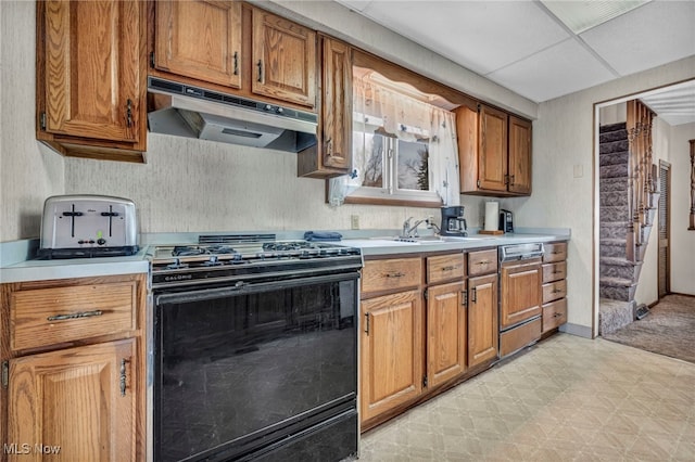 kitchen featuring brown cabinets, under cabinet range hood, paneled dishwasher, black gas range oven, and light countertops