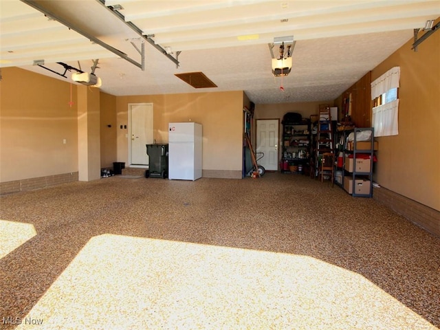 garage with a garage door opener, baseboards, and freestanding refrigerator