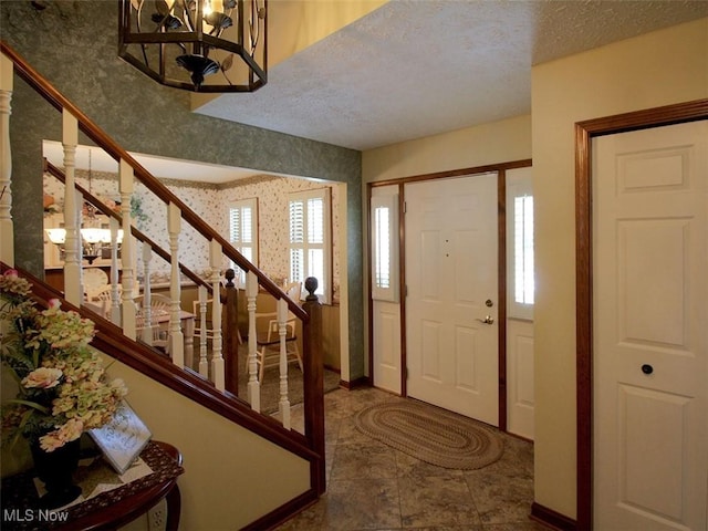 foyer with a textured ceiling, wallpapered walls, stairs, and baseboards