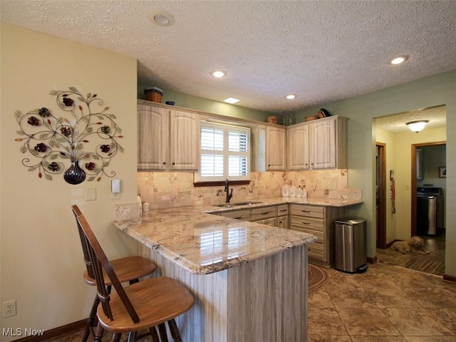 kitchen featuring light brown cabinetry, decorative backsplash, a peninsula, a kitchen breakfast bar, and a sink