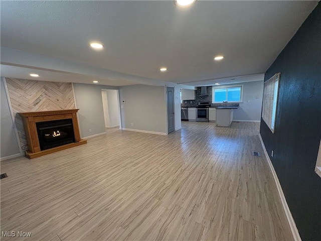 unfurnished living room with light wood-style floors, visible vents, a warm lit fireplace, and baseboards