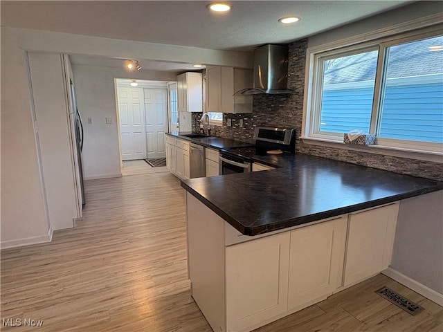 kitchen featuring light wood-type flooring, visible vents, dark countertops, appliances with stainless steel finishes, and wall chimney range hood