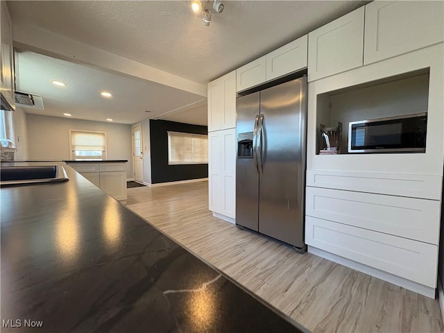 kitchen with light wood-style flooring, a sink, white cabinets, dark countertops, and stainless steel fridge