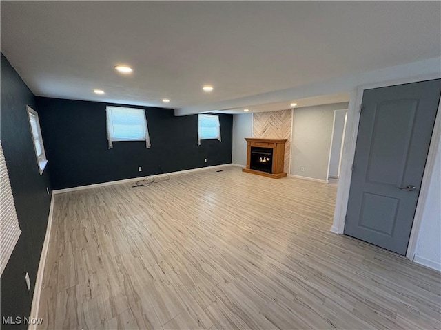 interior space featuring light wood-style floors, baseboards, and a warm lit fireplace