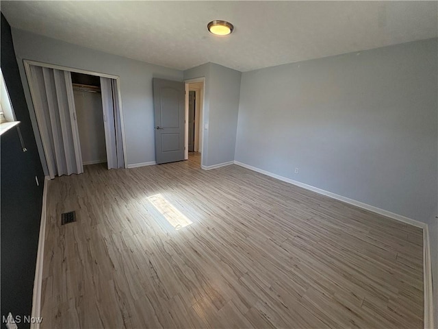 unfurnished bedroom featuring visible vents, wood finished floors, baseboards, and a closet