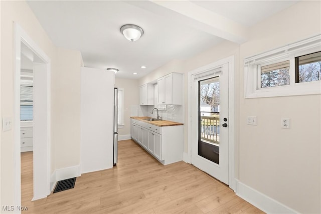 kitchen featuring visible vents, beamed ceiling, a sink, backsplash, and light wood finished floors