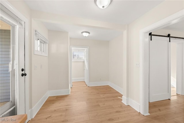 hallway featuring light wood finished floors, baseboards, and a barn door