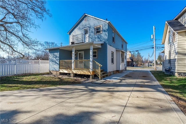 back of property featuring concrete driveway, a balcony, fence, and covered porch