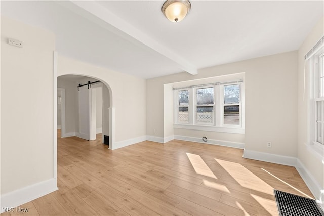 unfurnished room with light wood-type flooring, beam ceiling, a barn door, arched walkways, and baseboards