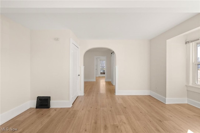 unfurnished room with light wood-style floors, a healthy amount of sunlight, and arched walkways