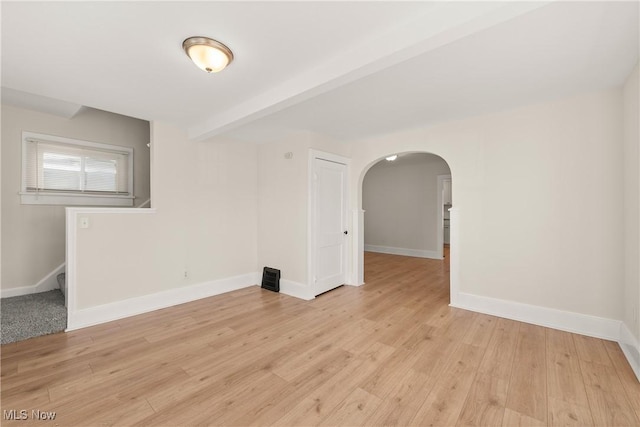 spare room featuring arched walkways, beam ceiling, light wood finished floors, and baseboards