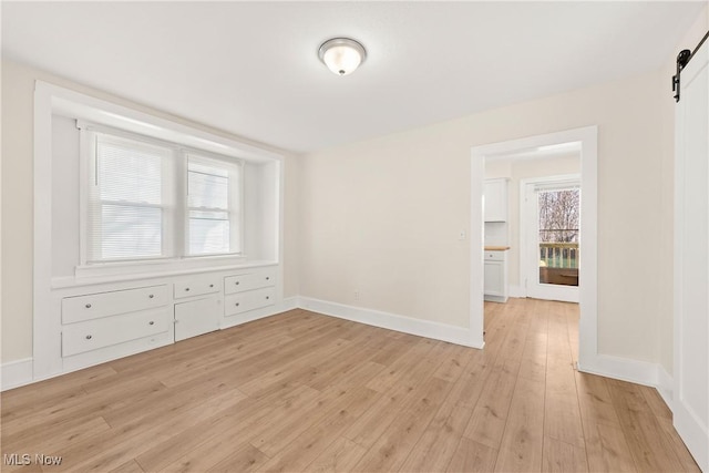 spare room with a barn door, baseboards, and light wood-style flooring