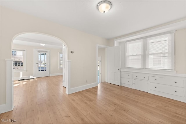 unfurnished room with baseboards, arched walkways, and light wood-style flooring