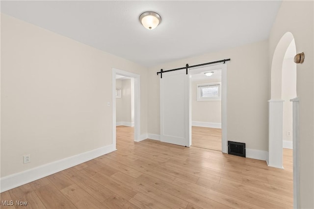 spare room featuring arched walkways, visible vents, baseboards, and light wood-style floors