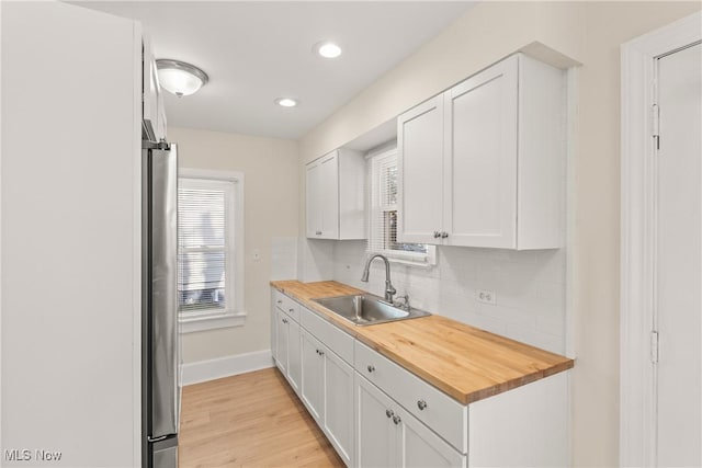 kitchen with freestanding refrigerator, a sink, wood counters, white cabinetry, and tasteful backsplash