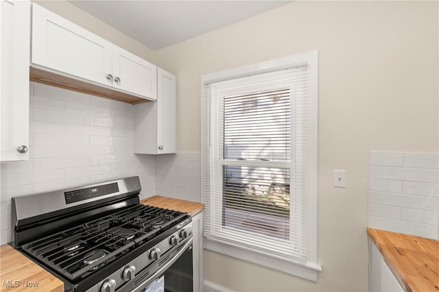 kitchen with white cabinetry, backsplash, stainless steel gas range, and butcher block countertops