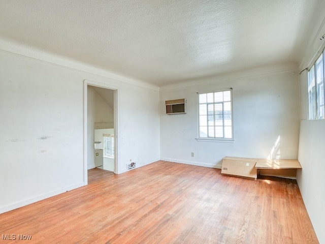 spare room featuring light wood finished floors, a textured ceiling, an AC wall unit, and baseboards