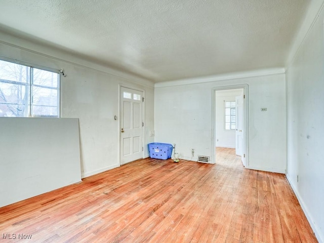 empty room with light wood-type flooring, a textured ceiling, and visible vents