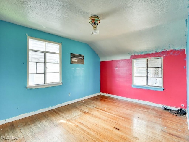 bonus room with baseboards, a wall mounted AC, lofted ceiling, wood-type flooring, and a textured ceiling